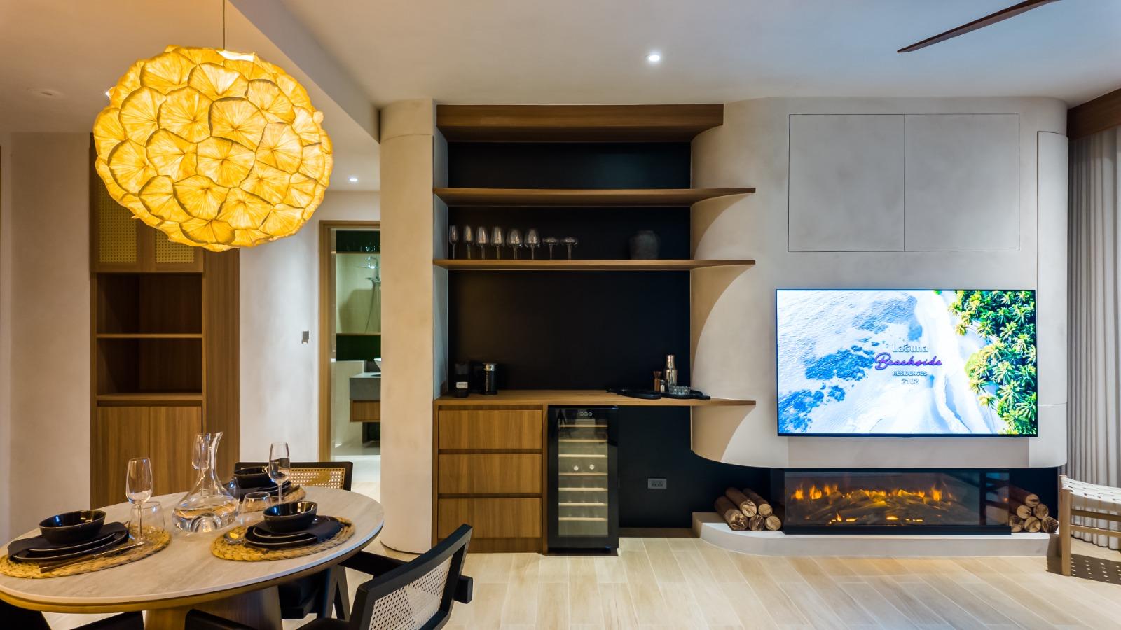 Contemporary dining and living area with a round table set for four, a large yellow pendant lamp, and a built-in entertainment wall with a fireplace and TV.
