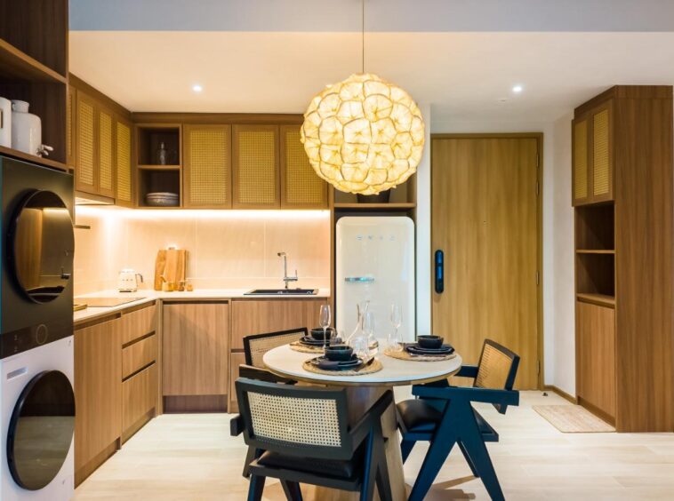 Open-plan kitchen with warm wood cabinets, round dining table for four, and a large woven pendant light overhead.