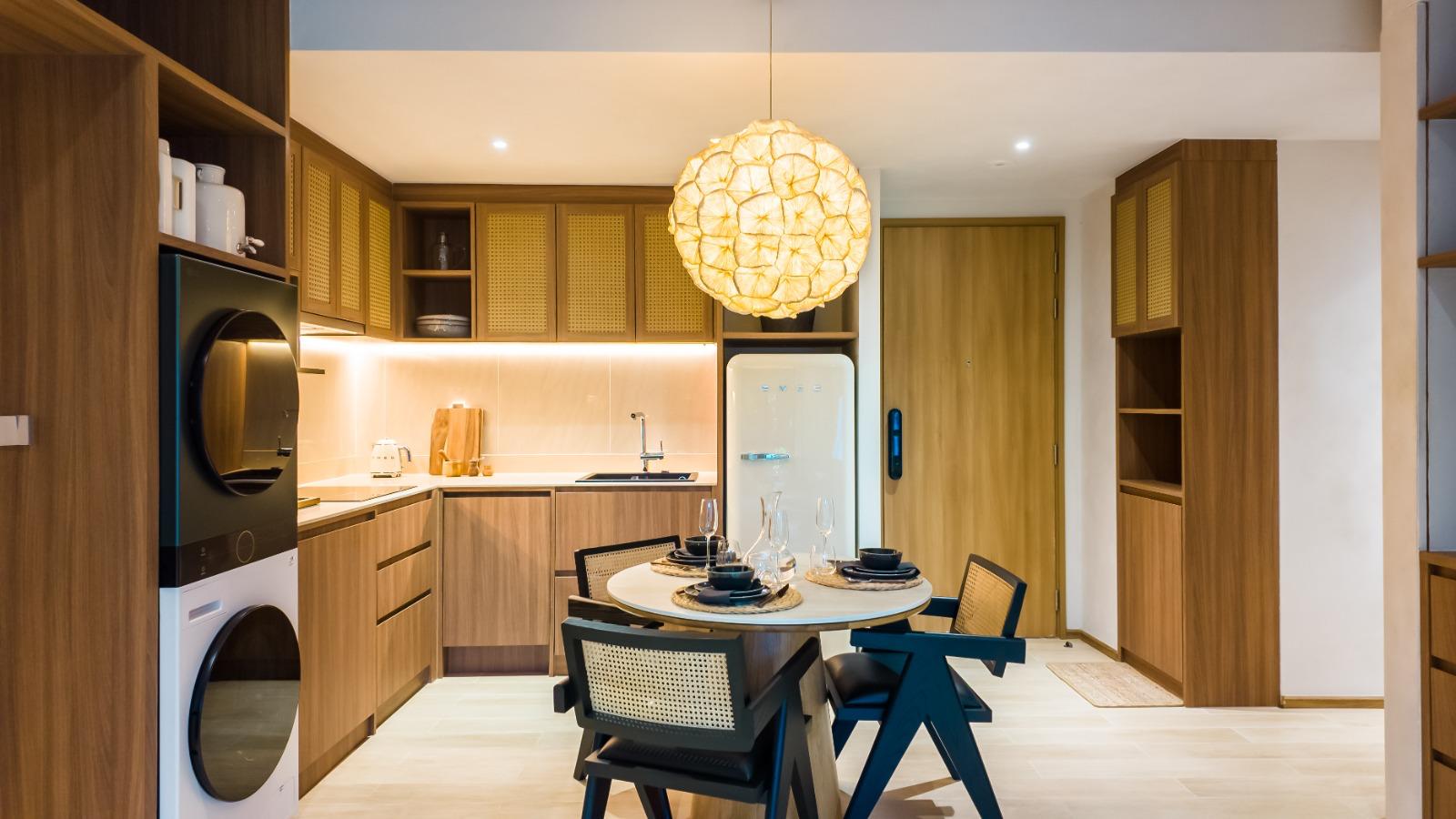 Open-plan kitchen with warm wood cabinets, round dining table for four, and a large woven pendant light overhead.
