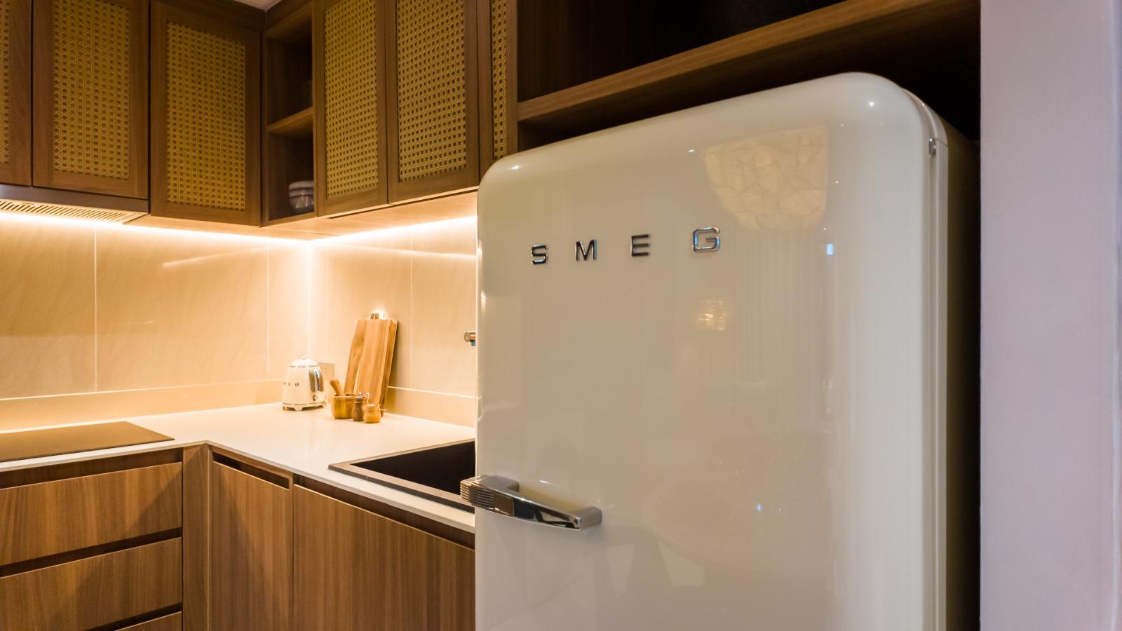 Cream SMEG refrigerator with chrome handle in a warm, wood-toned kitchen under recessed lighting.