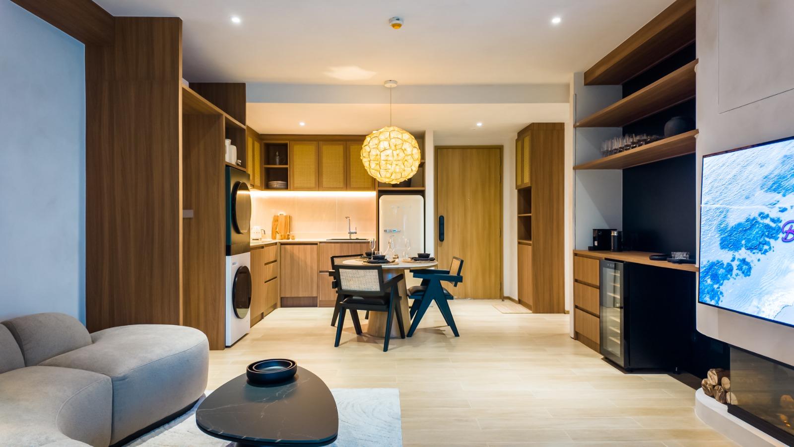 Open-concept living area with wooden kitchen cabinets, round woven pendant light, and a dining table at center.