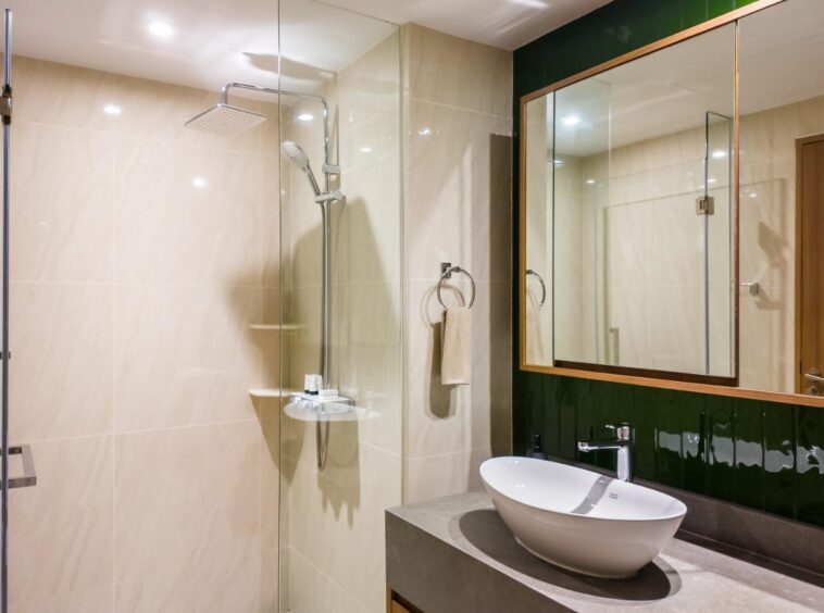 Modern bathroom with a glass-enclosed shower, beige tiled walls, and a white vessel sink on a dark countertop.