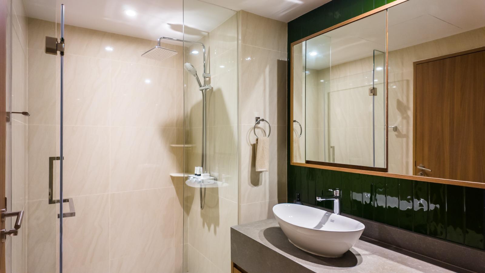 Modern bathroom with a glass-enclosed shower, beige tiled walls, and a white vessel sink on a dark countertop.