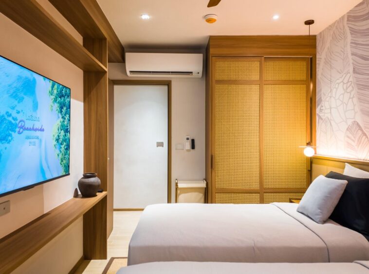 Hotel room with two single beds, a wall-mounted flat-screen TV, and a wooden console beneath it.
