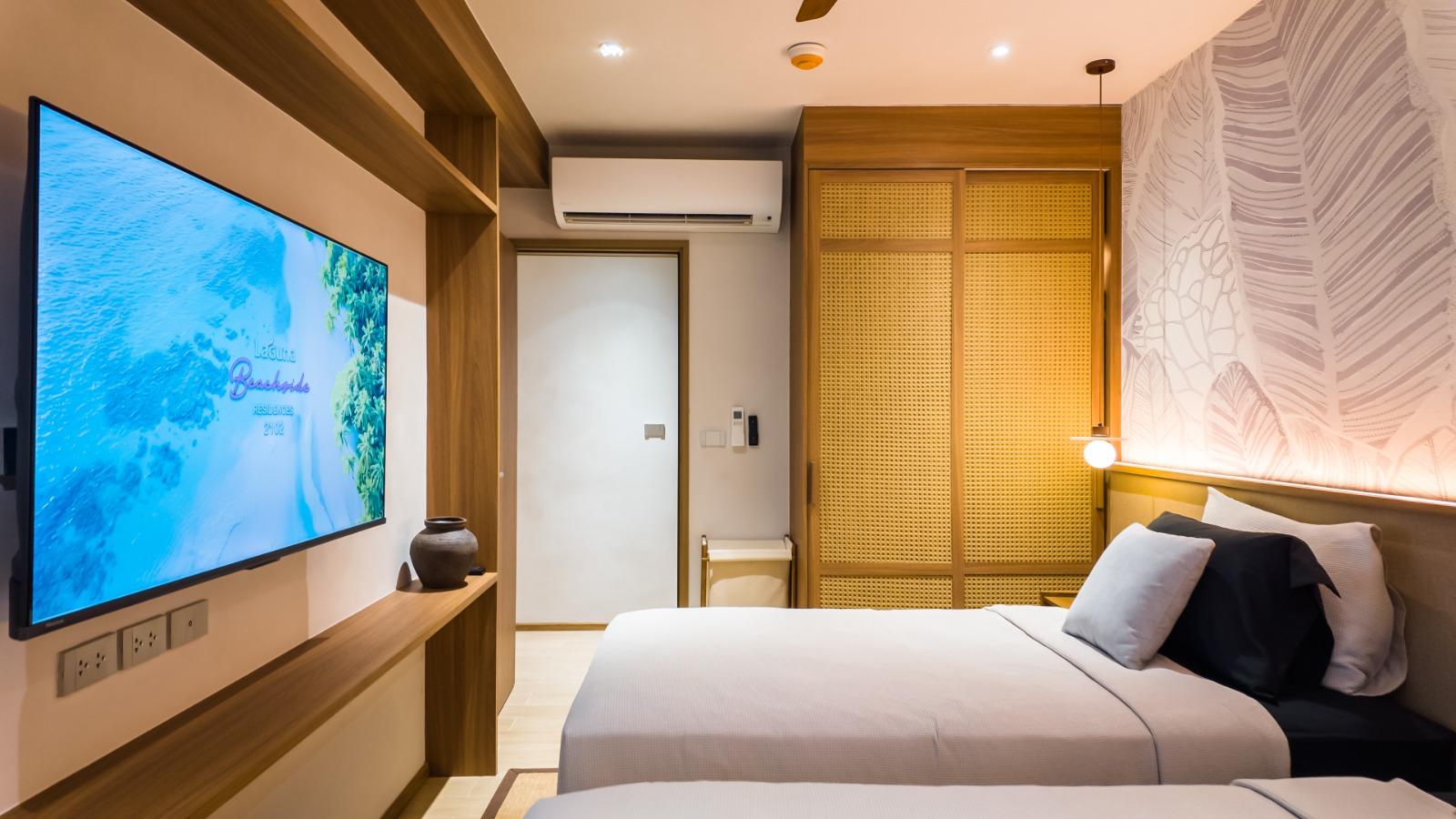 Hotel room with two single beds, a wall-mounted flat-screen TV, and a wooden console beneath it.