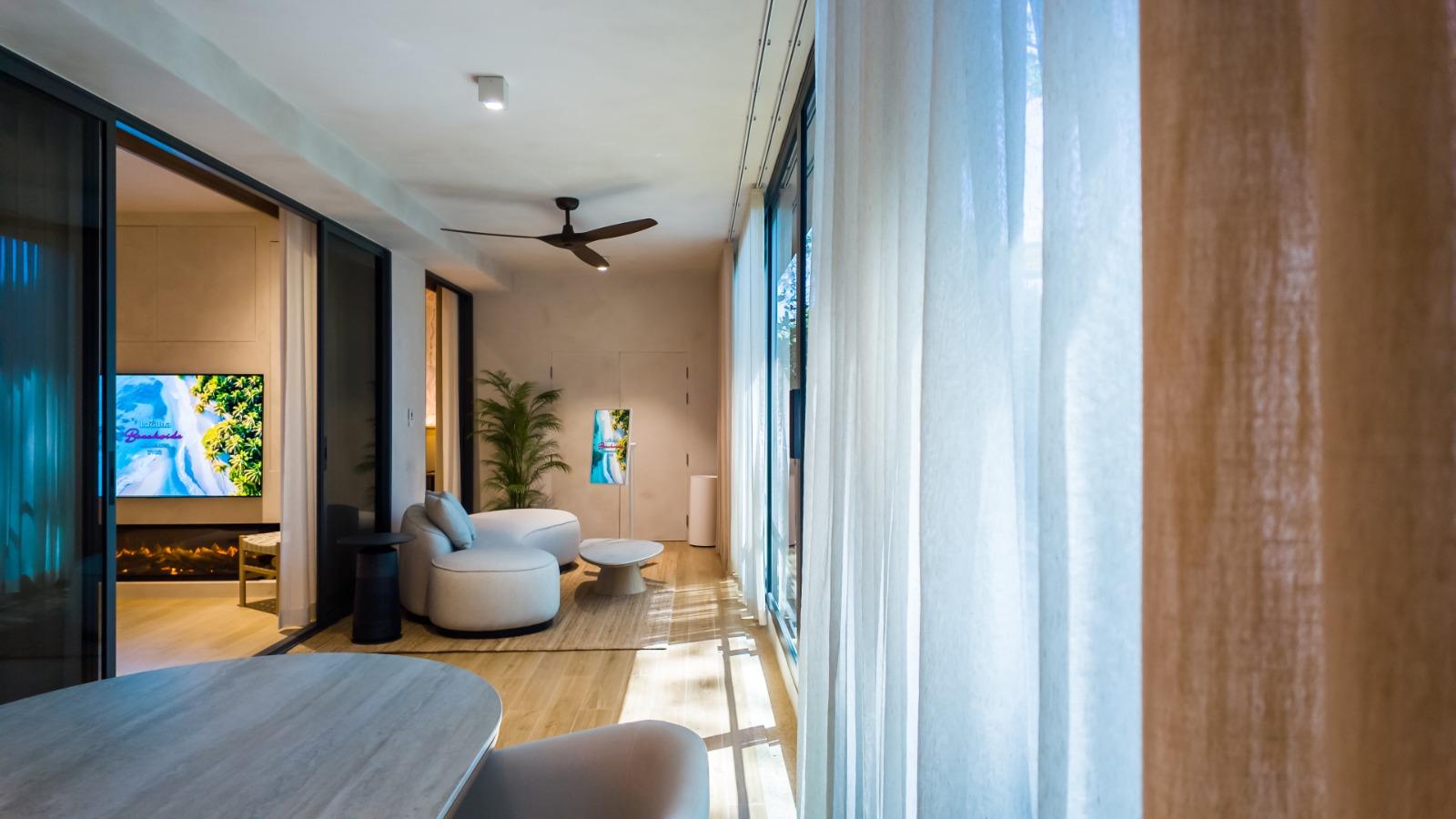 Bright modern living room with large floor-to-ceiling windows, sheer white curtains, and a curved white sofa with a coffee table in the center.