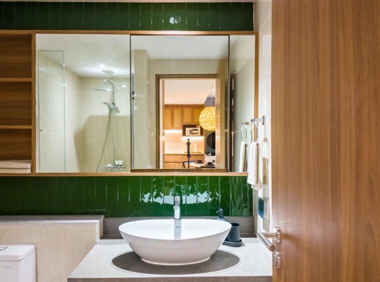 Modern bathroom with a round white vessel sink on a gray countertop, and a green tiled backsplash with a large mirror above it.