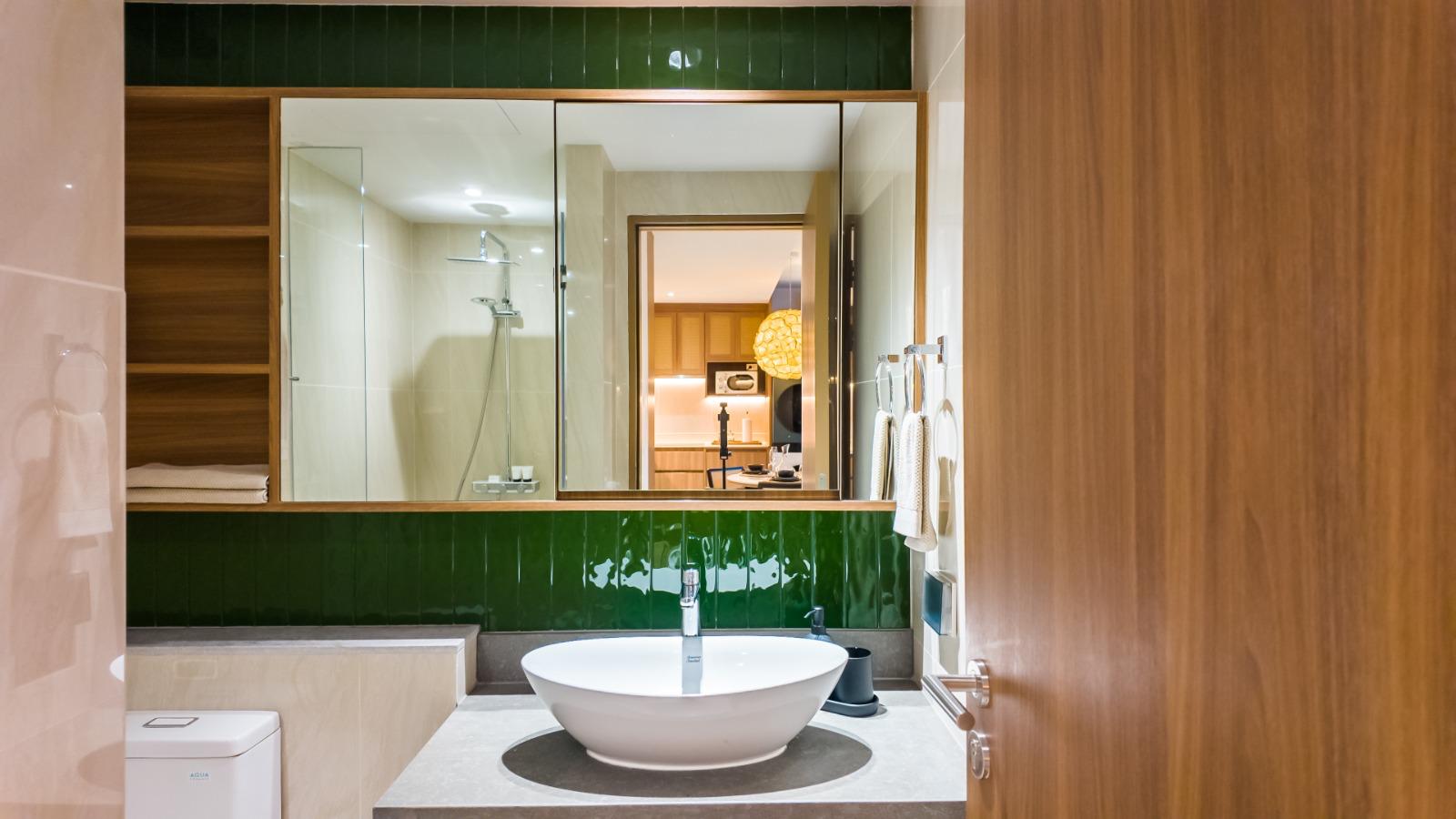 Modern bathroom with a round white vessel sink on a gray countertop, and a green tiled backsplash with a large mirror above it.