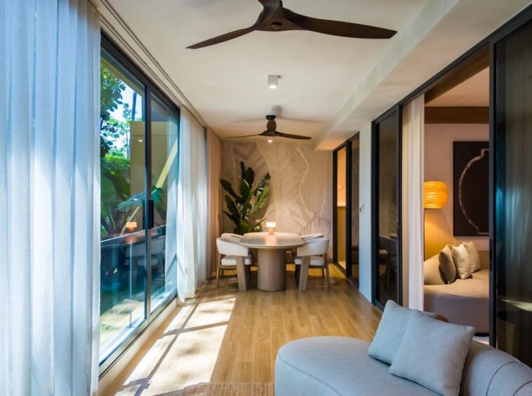Bright, modern living space with a circular dining table and four chairs, sunlit through large glass doors to an outdoor area.