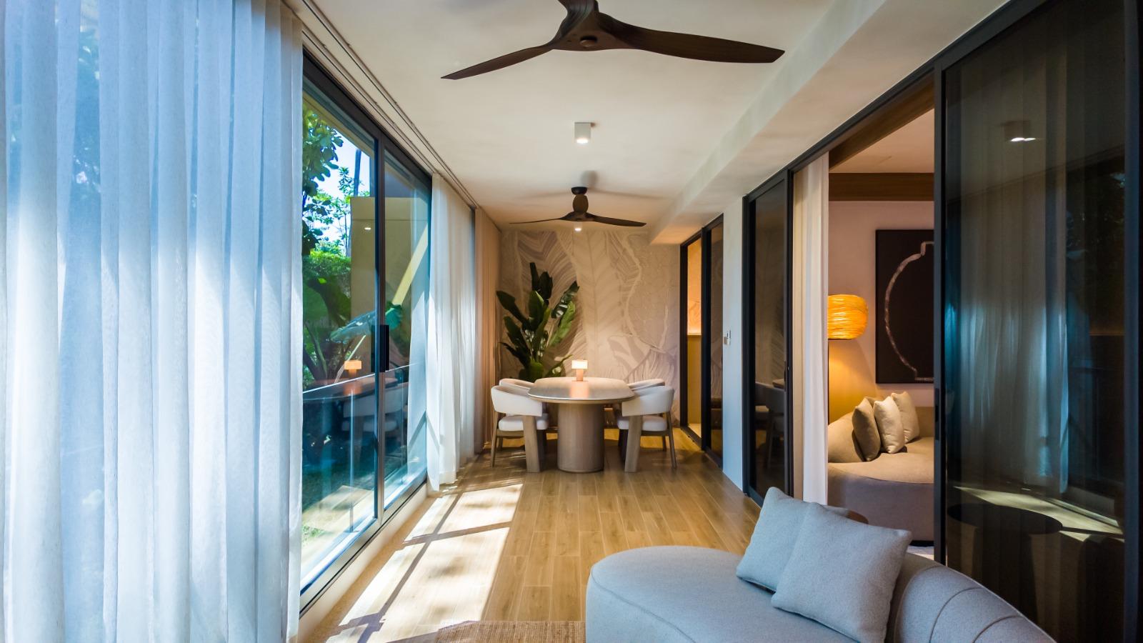 Bright, modern living space with a circular dining table and four chairs, sunlit through large glass doors to an outdoor area.