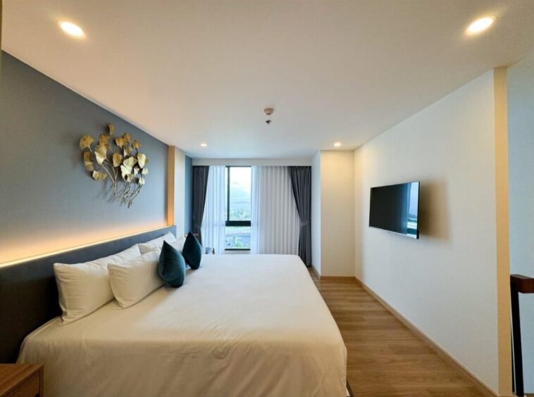Bright hotel room with a large white bed, dark headboard and blue accent wall with metal leaf art.