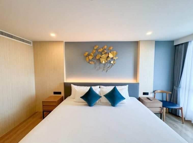 Hotel bedroom with a large white bed, teal throw pillows, wooden nightstands, and blue accent wall with gold wall art.