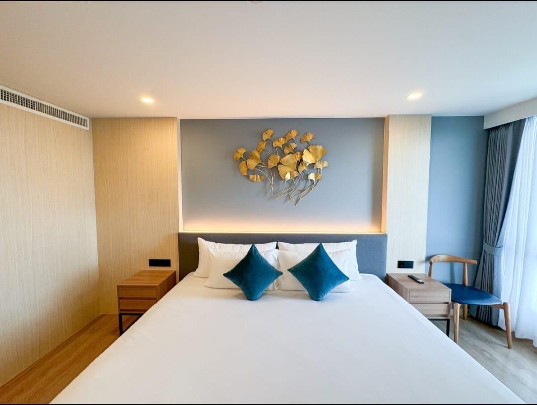 Hotel bedroom with a large white bed, teal throw pillows, wooden nightstands, and blue accent wall with gold wall art.