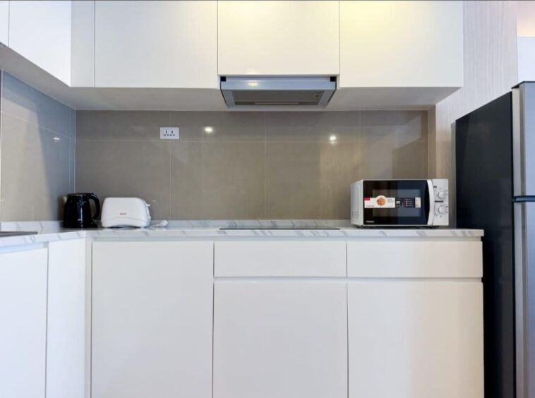 Modern white kitchen with grey tile backsplash: microwave on the counter, toaster and kettle on the left, refrigerator on the right.
