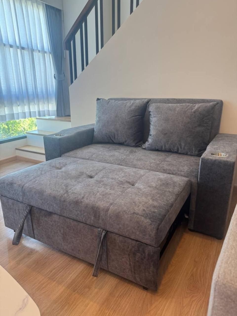 Gray fabric sofa with a chaise lounge and two back cushions in a bright living room by a large window with blue curtains.