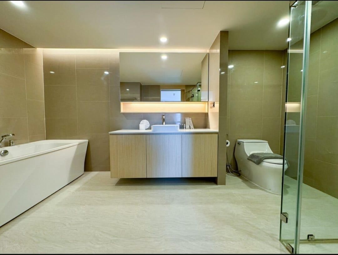 A contemporary bathroom with a freestanding white bathtub on the left, a wood vanity with sink and mirror in the center, and a toilet on the right behind a glass shower wall.