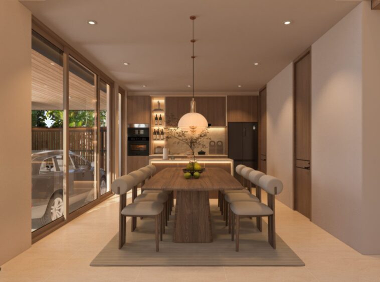 Open-plan dining kitchen with a long wooden table, white padded stools, and a pendant light, flanked by tall glass doors to a patio outside.