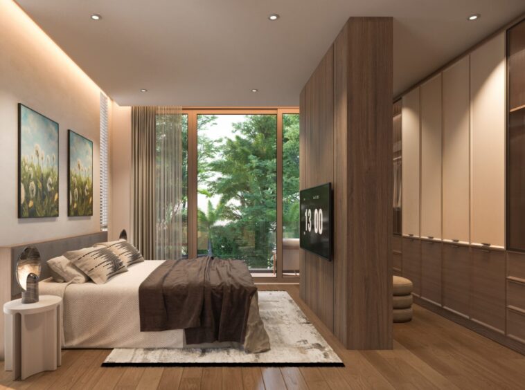 Modern bedroom with a large window showing greenery, a bed with neutral bedding, and a wood-paneled divider separating a wall-mounted TV from built-in wardrobes.