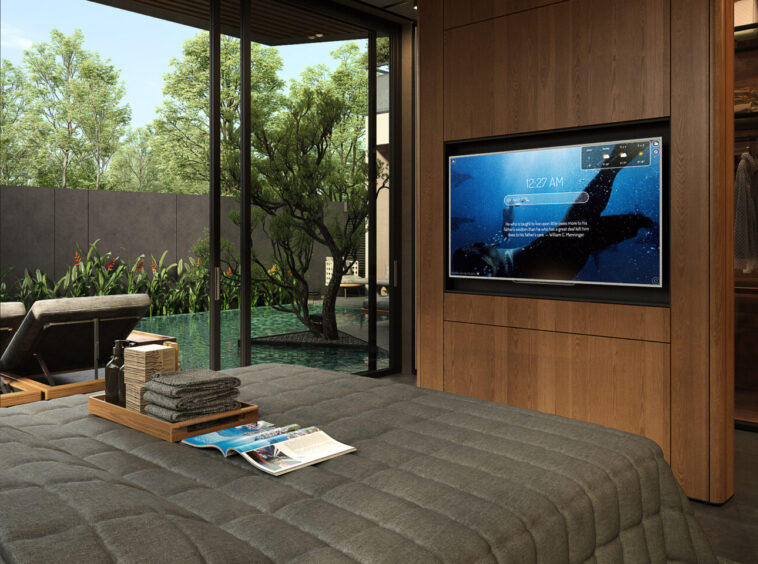 Modern bedroom with floor-to-ceiling glass walls overlooking a pool and greenery; a TV is mounted in a wood-paneled wall.