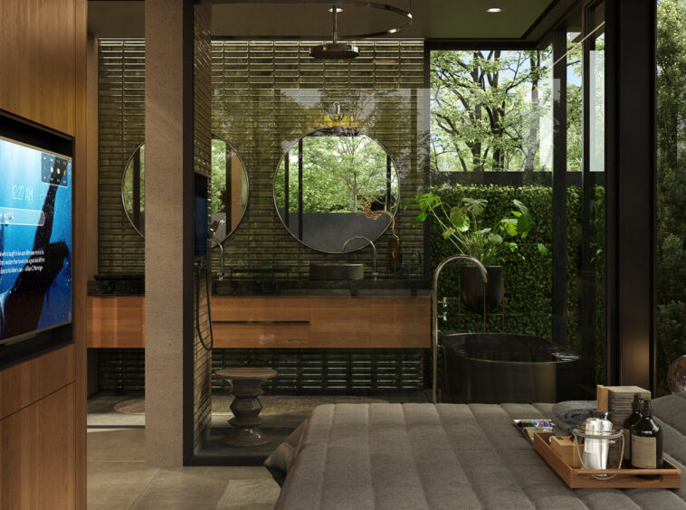 Luxurious hotel bedroom with a glass-walled ensuite, circular mirrors, and a drinks tray on the bed overlooking greenery outside.