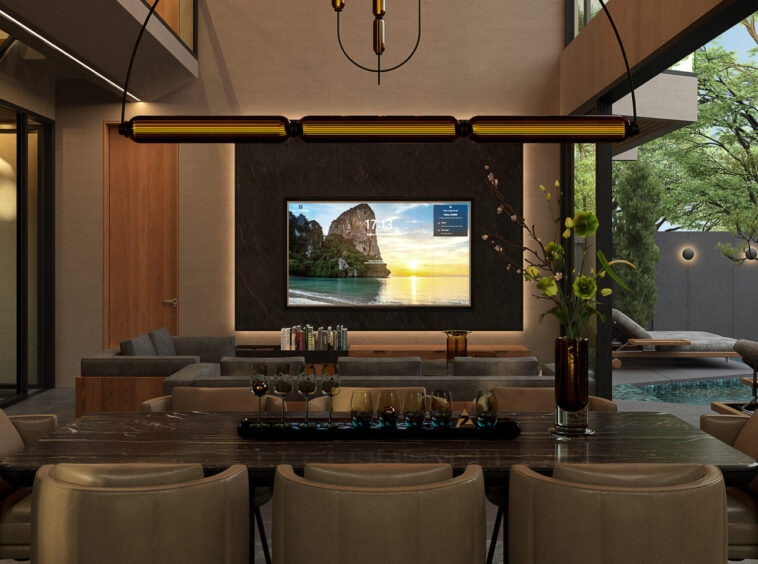 Luxurious living room with a wall-mounted TV on a dark marble backdrop, a long dining table in the foreground, and beige chairs around it, overlooking an outdoor pool and greenery.