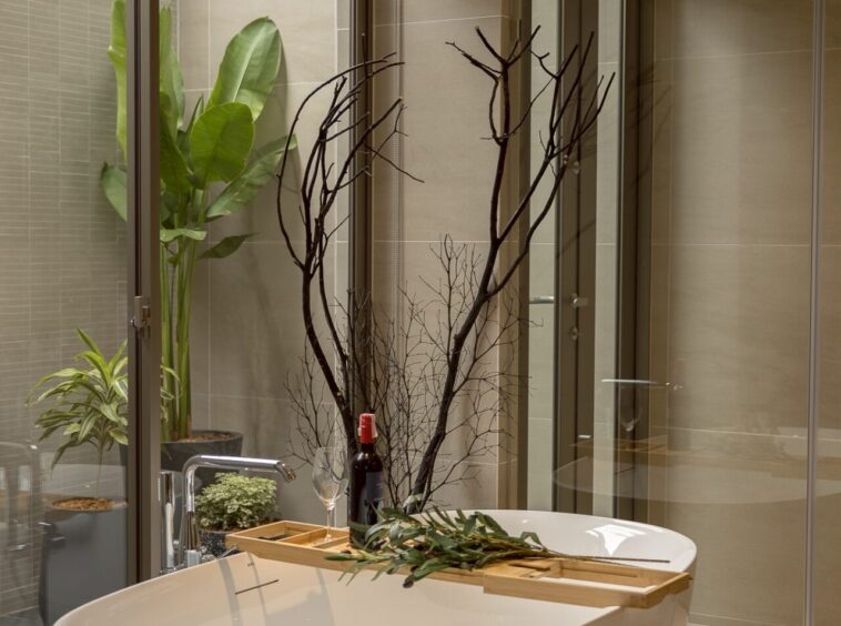 Modern bathroom featuring a white freestanding tub with a wooden tray holding wine, glass, and greenery, beside a glass shower enclosure.