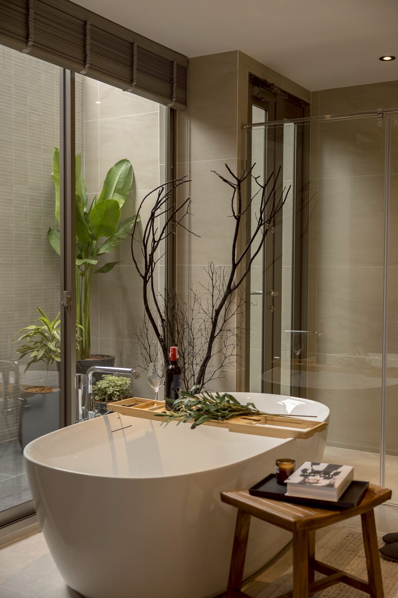 Modern bathroom featuring a white freestanding tub with a wooden tray holding wine, glass, and greenery, beside a glass shower enclosure.