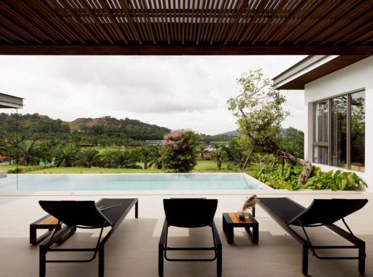 Poolside lounge area with four black chairs and a small table, overlooking a green landscape and distant hills.