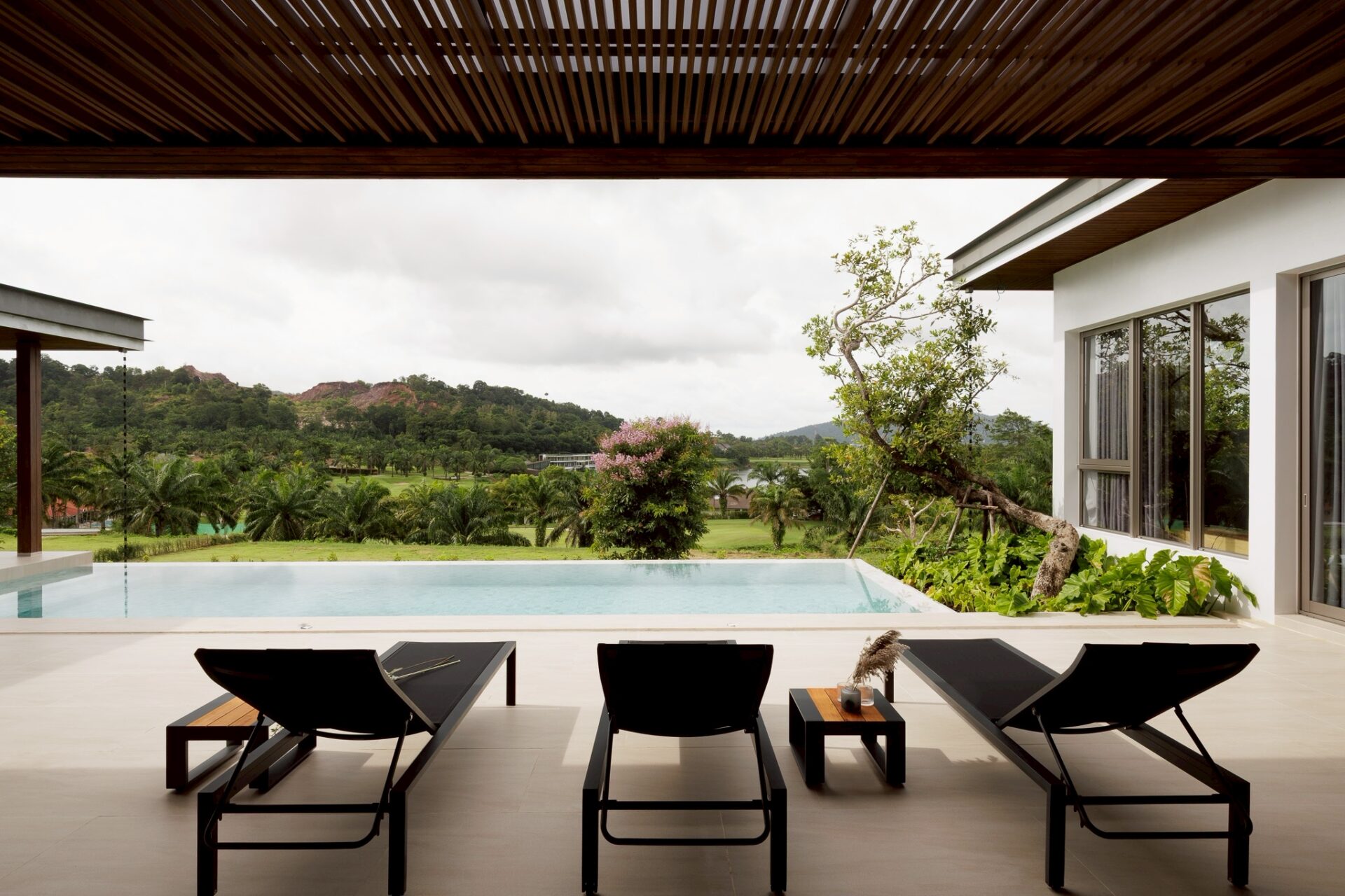 Poolside lounge area with four black chairs and a small table, overlooking a green landscape and distant hills.