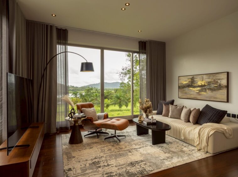 Living room with a beige sectional, black coffee table, and leather lounge chair facing a large window view of trees and hills.