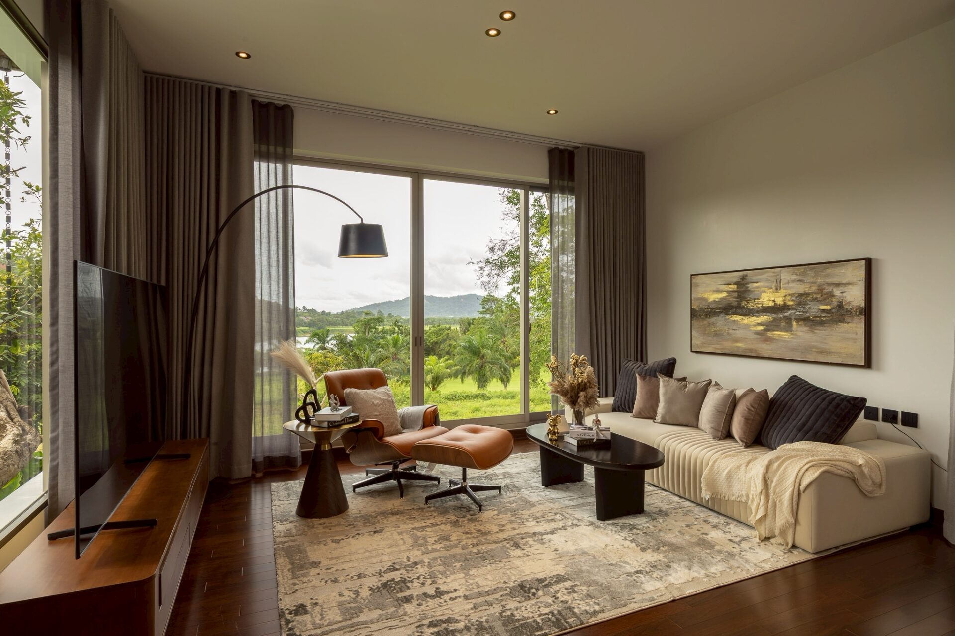 Living room with a beige sectional, black coffee table, and leather lounge chair facing a large window view of trees and hills.