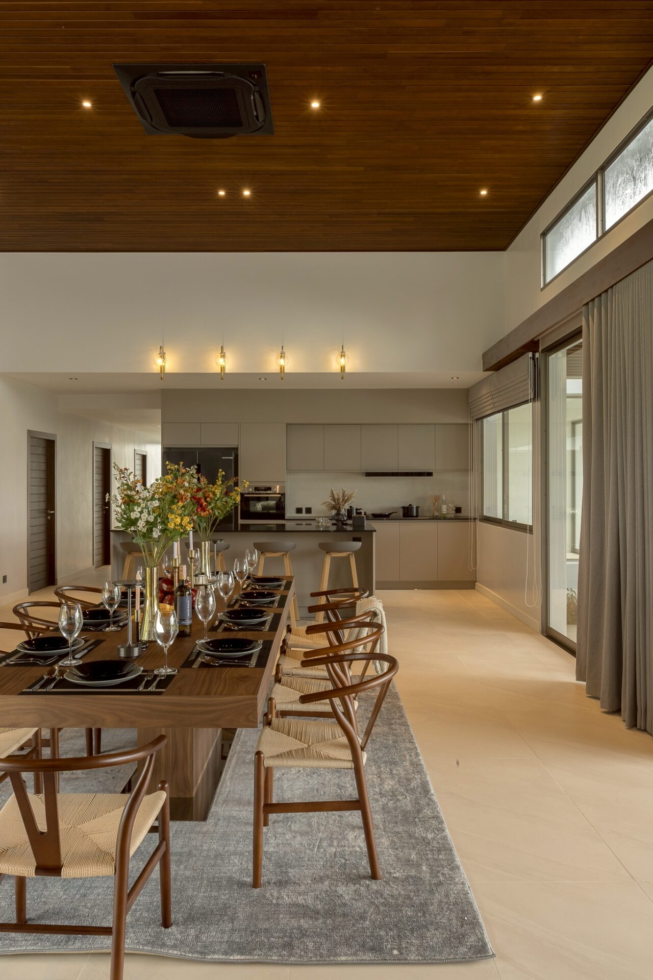 Open dining area with a long wooden table set for a formal dinner, flowers, and wine, with a modern kitchen in the background.