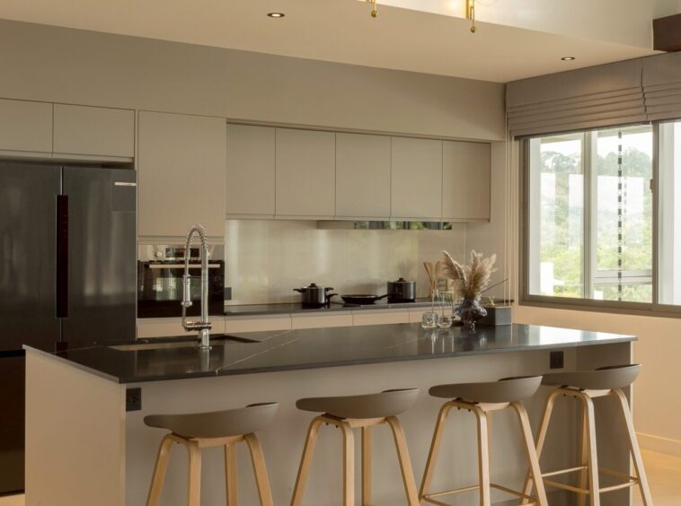 Modern kitchen with a gray island, four wooden bar stools, stainless appliances, and brass globe pendant lights.