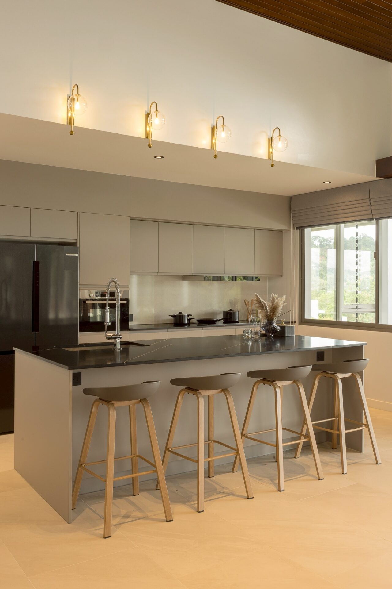 Modern kitchen with a gray island, four wooden bar stools, stainless appliances, and brass globe pendant lights.
