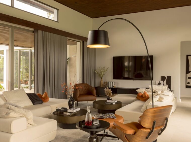 Contemporary living room with a cream sectional sofa, black circular coffee tables, orange cushions, and a large curved arc floor lamp.