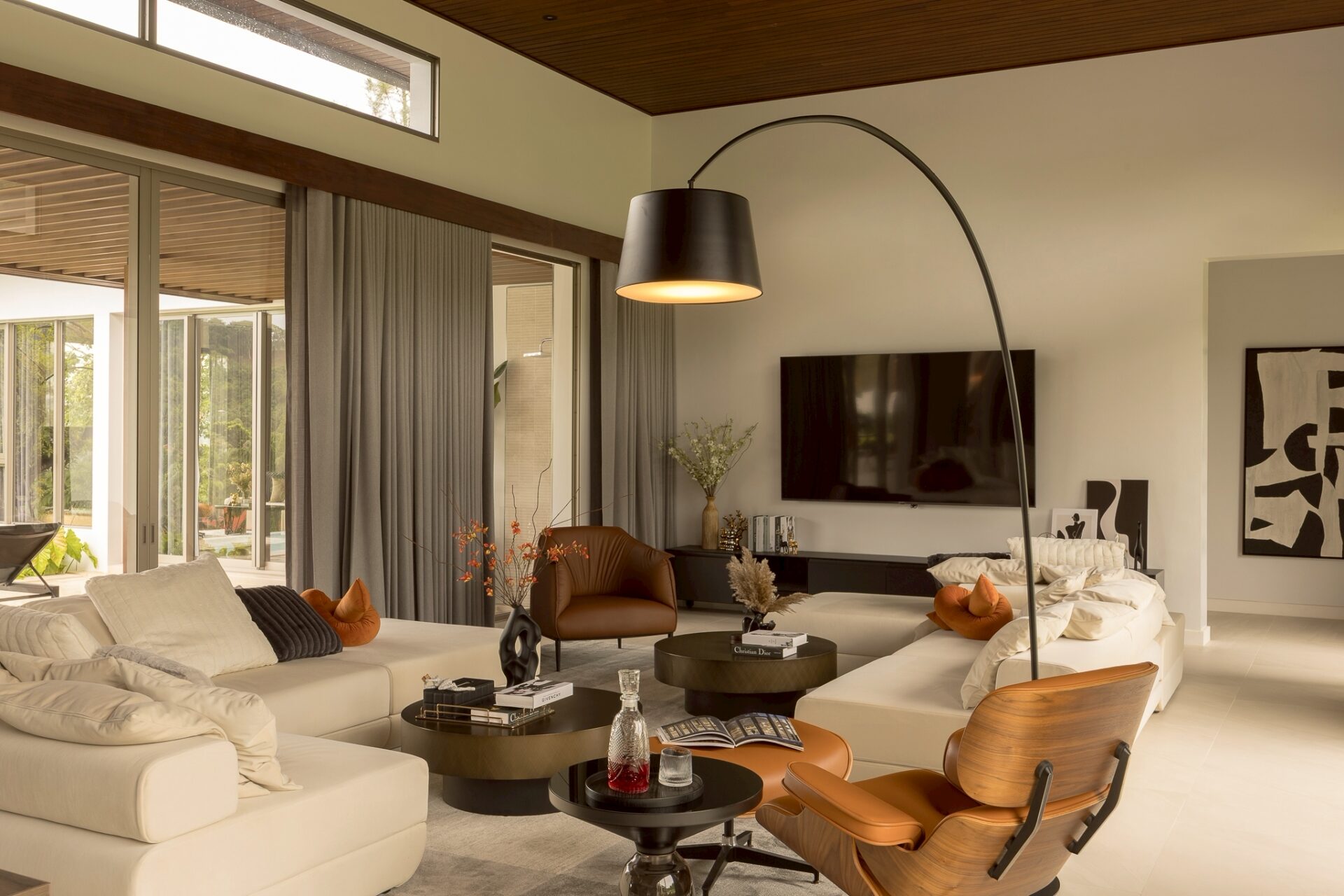 Contemporary living room with a cream sectional sofa, black circular coffee tables, orange cushions, and a large curved arc floor lamp.