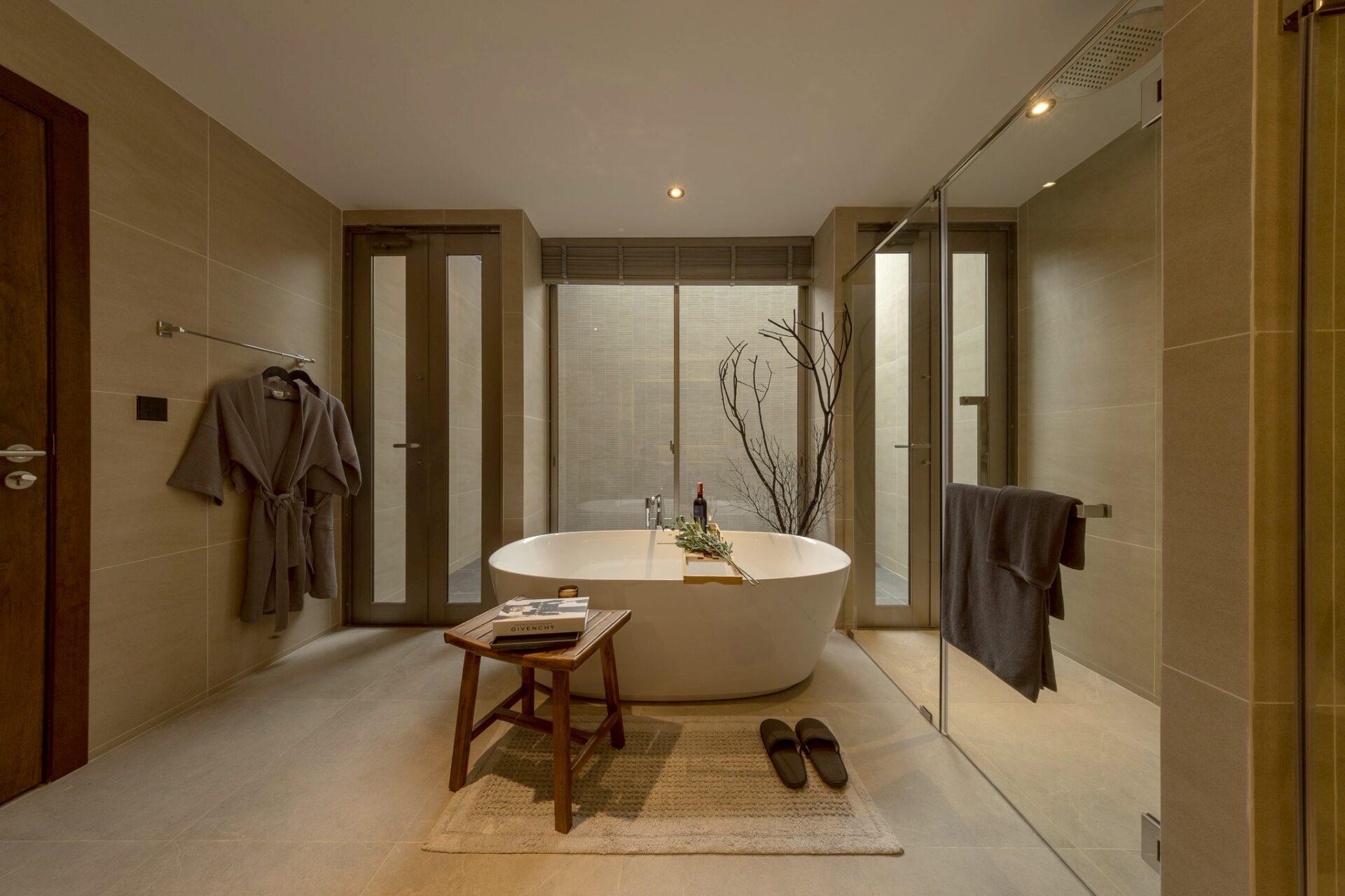 Modern spa bathroom with a freestanding tub on a rug, a wooden stool with magazines, and a glass-walled shower.