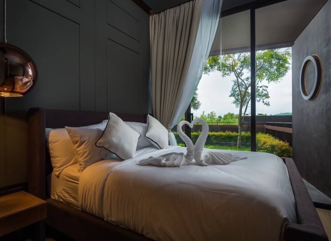 Bed with white linens and two towel swans on top, in a modern hotel room with floor-to-ceiling windows and a garden view.