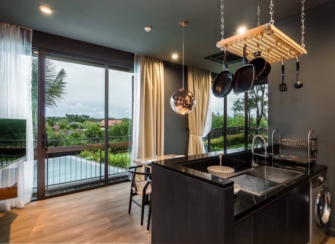 Modern kitchen with a black island, hanging pot rack, and large glass doors opening to a balcony with greenery outside.