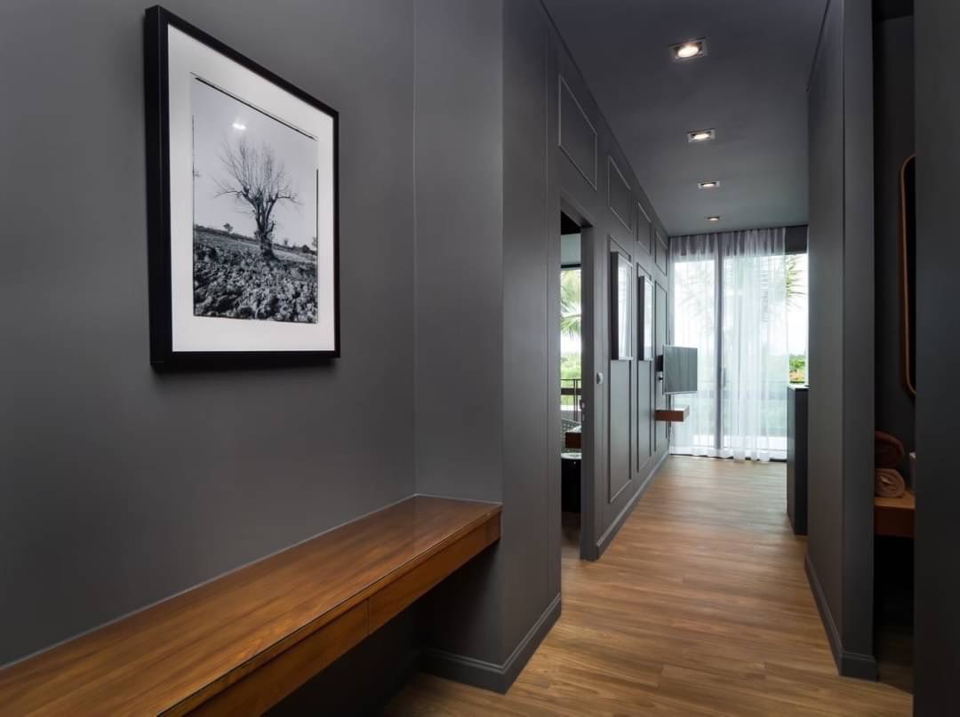 Gray modern hallway with a wooden bench, a framed black-and-white tree photograph, and sheer-curtained windows at the far end.