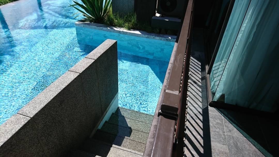 Corner of a bright blue pool with a short stone wall and steps leading into the water beside a balcony and sliding glass door.