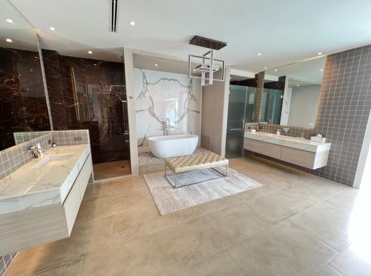 Luxurious bathroom with a freestanding oval tub in a marble alcove, twin vanities, and a glass-walled shower.