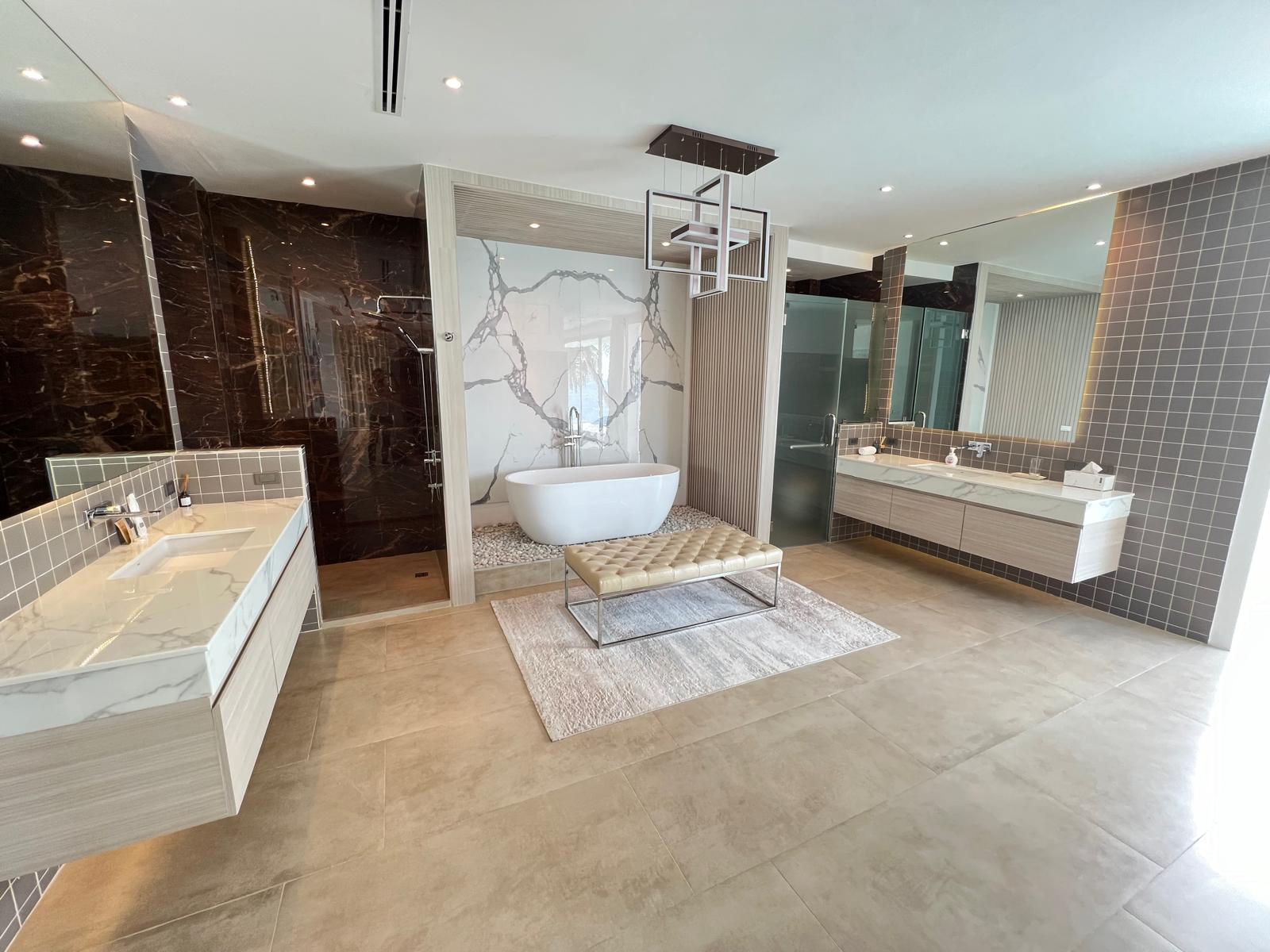 Luxurious bathroom with a freestanding oval tub in a marble alcove, twin vanities, and a glass-walled shower.