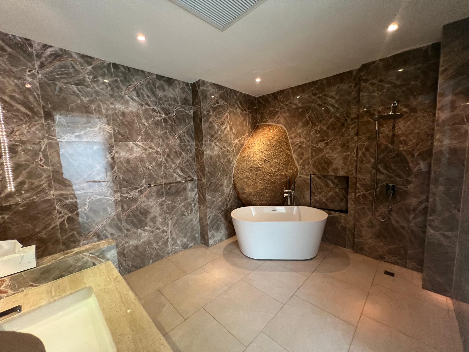 Luxurious bathroom with dark marble walls, a white freestanding bathtub, and a large stone sculpture behind it