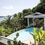 Infinity pool with a tropical garden and an ocean view, plus a shaded gazebo and lounge seating nearby.