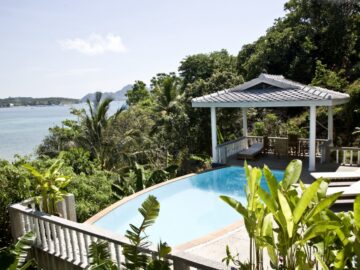 Infinity pool with a tropical garden and an ocean view, plus a shaded gazebo and lounge seating nearby.