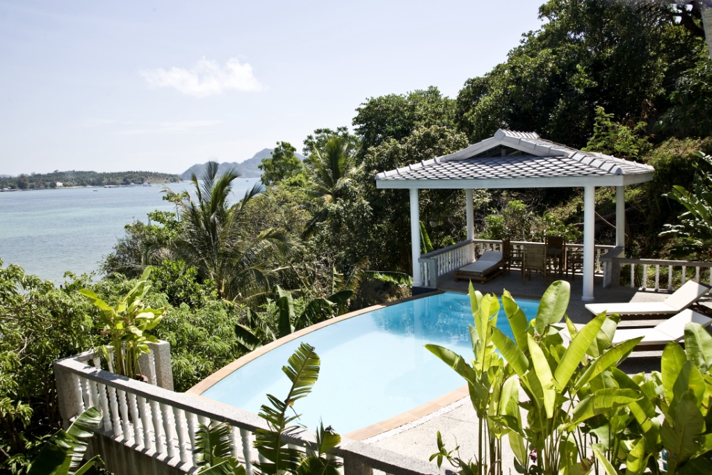 Infinity pool with a tropical garden and an ocean view, plus a shaded gazebo and lounge seating nearby.