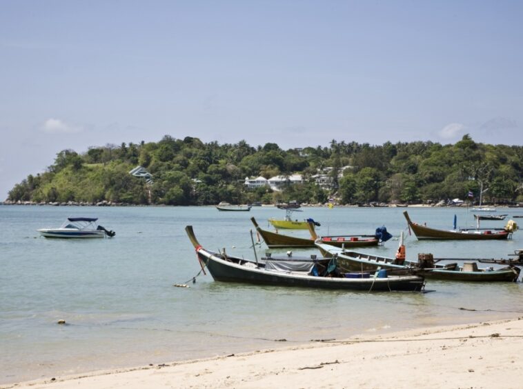 Small boats anchored near a sandy beach with a forested island in the background.