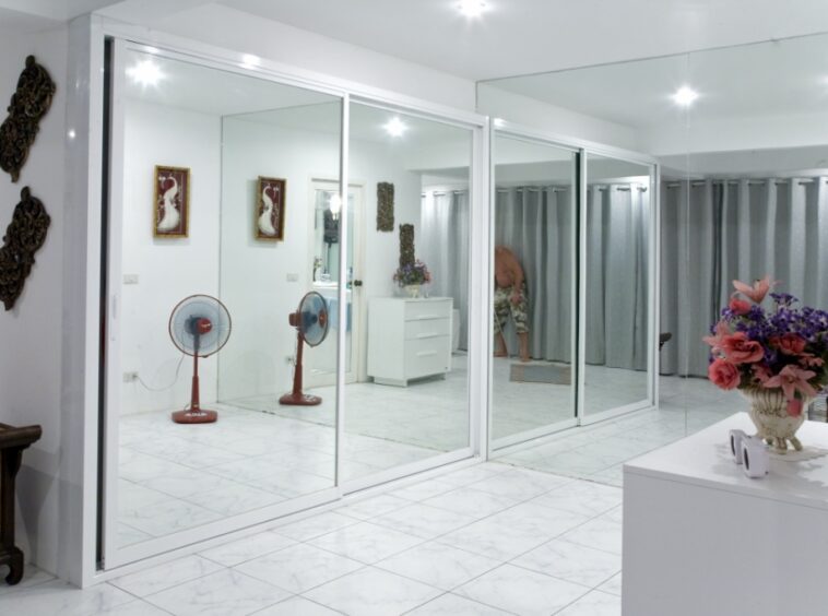 Bright interior with large sliding glass doors dividing a white-tiled room, fans, and a person bending near gray curtains in the back.