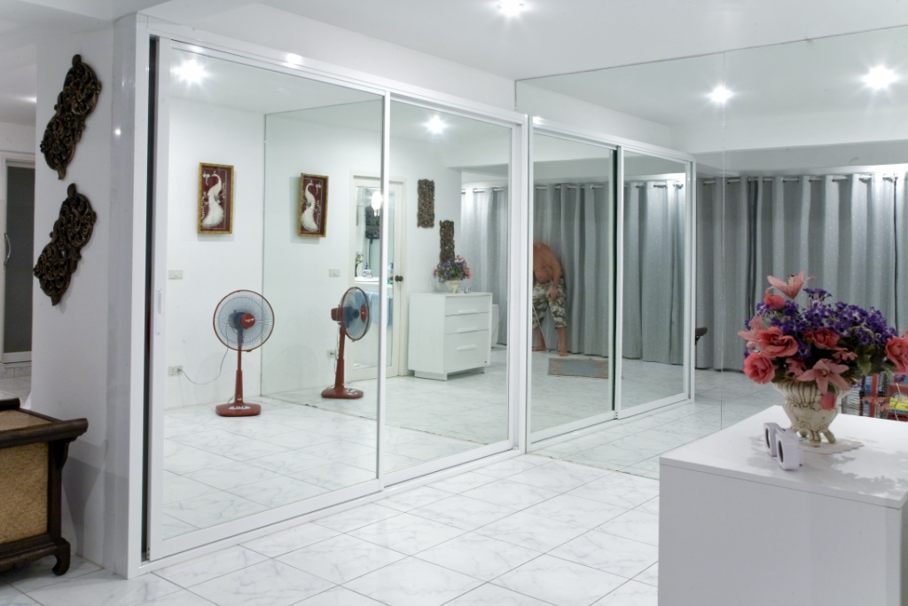 Bright interior with large sliding glass doors dividing a white-tiled room, fans, and a person bending near gray curtains in the back.